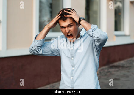 Portrait of young angry man with hands on head. Clings to his head and shouts Stock Photo