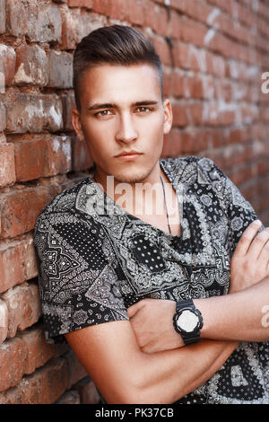 Handsome young guy from America stands on the brick wall background. Stock Photo