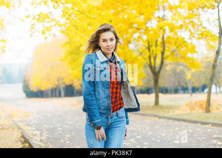 Pretty girl in jeans clothes and a red checkered shirt in autumn park. Stock Photo