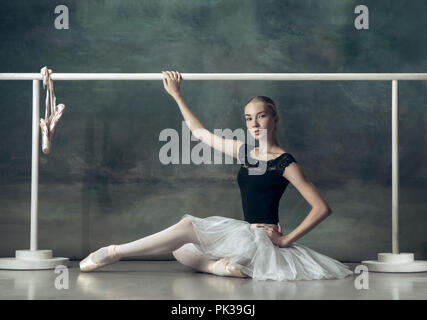 The classic ballet dancer in white tutu posing at ballet barre on studio background. Young teen before dancing. Ballerina project with caucasian model. The ballet, dance, art, contemporary, choreography concept Stock Photo