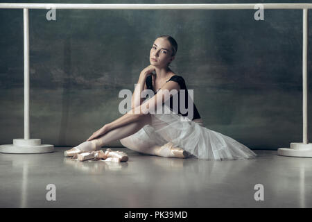 The classic ballet dancer in white tutu posing at ballet barre on studio background. Young teen before dancing. Ballerina project with caucasian model. The ballet, dance, art, contemporary, choreography concept Stock Photo