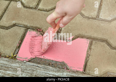 House painter paints the tile on the garden path using a paint brush. Stock Photo
