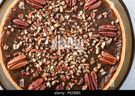 Pecan Pie, made from butter enriched pastry with golden syrup, maple sauce and breadcrumbs, topped with pecans on grey background Stock Photo