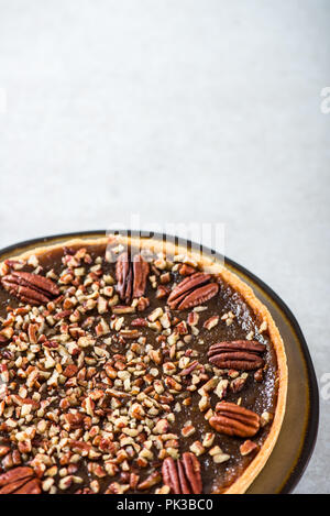 Pecan Pie, made from butter enriched pastry with golden syrup, maple sauce and breadcrumbs, topped with pecans on grey background Stock Photo