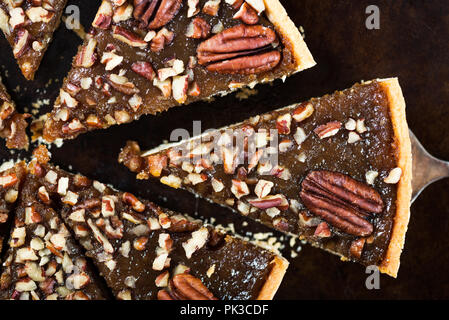 Pecan Pie, made from butter enriched pastry with golden syrup, maple sauce and breadcrumbs, topped with pecans, on dark background Stock Photo