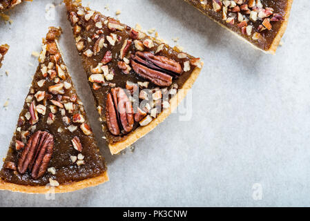 Pecan Pie, made from butter enriched pastry with golden syrup, maple sauce and breadcrumbs, topped with pecans on grey background Stock Photo