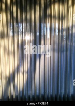 Tree shadows falling onto window curtains with folds and textures. Stock Photo