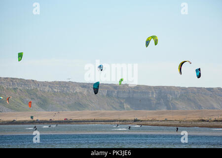 Kite surfers on a sunny day in Portland Harbour at low tide near Weymouth in Dorset. Behind them is the back of Chesil beach and beyond that the cliff Stock Photo
