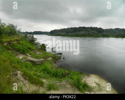 calm river, one grassy bank and forest on other side, covered with lowering clouds Stock Photo
