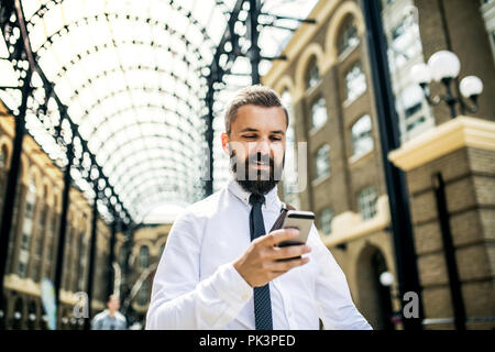 Businessman with smartphone on the trian station in London, text messaging. Stock Photo
