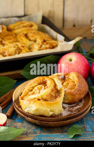 Fresh Homemade Rolls Buns with apples and cinnamon in glaze on a blue vintage wooden background. Stock Photo
