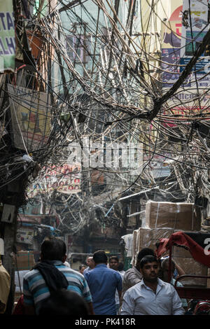 Pedestrians walking in narrow street with large tangled bird's nest of power cables overhead in Old Delhi, New Delhi, Delhi, India Stock Photo