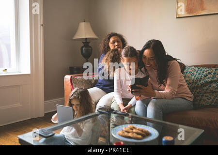 Grandmother is making hairstyle of granddaughter while using mobile with her mother Stock Photo