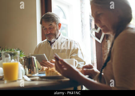 Senior couple using digital tablet and mobile phone while having breakfast Stock Photo