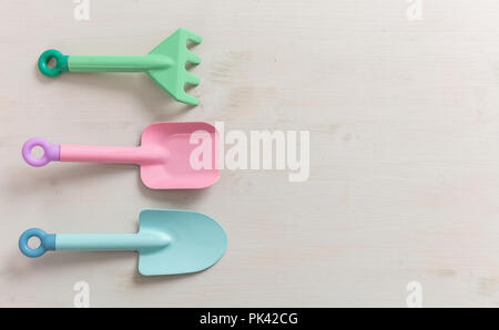 Toys and nature. Top view of children gardening tools in pastel colors on a white wooden board background with copy space, isolated. Stock Photo