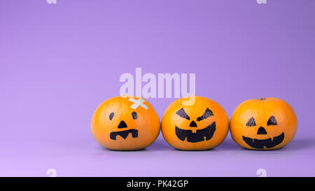 Three Fresh Oranges with Halloween Pumpkins painted face.  Easy DIY decoration for Halloween festival on violet background Stock Photo