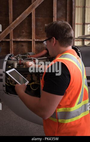 Mechanic using digital tablet while servicing aircraft engine Stock Photo
