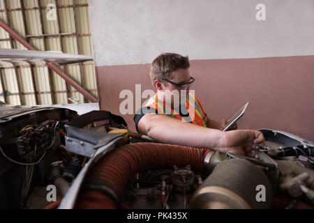 Mechanic using digital tablet while servicing aircraft engine Stock Photo