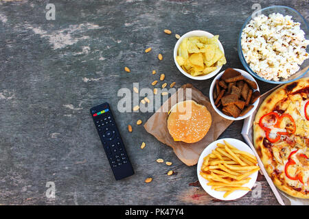 TV remote control, fast food on old wooden background. Concept of junk eating. Top view. Flat lay. Stock Photo