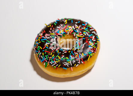 Top view studio photo of a delicious and tempting chocolate donut with colorful sprinkles isolated on white background in unhealthy nutrition and choc