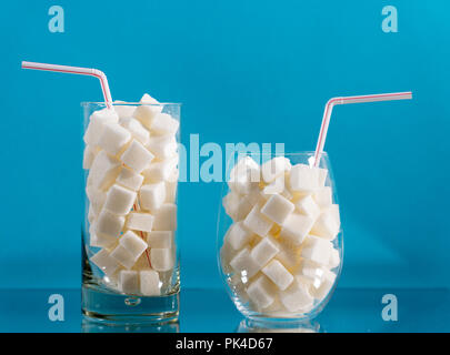 Glass with red stripes straw filled with sugar cubes on blue background. Junk food, unhealthy diet, sugar on refreshing drinks, nutrition concept. Stock Photo