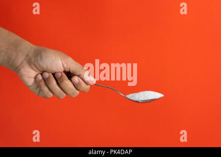 Woman hand holding and offering a spoon full of sugar isolated on a red background in sugar addiction, diet, health problems, diabetes, calories and q Stock Photo