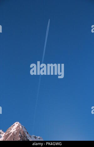 far away jet plane going up like a rocket launched behind a mountain, leaving a perfect contrail in a clear blue sky at the Alpes, Tignes, France Stock Photo