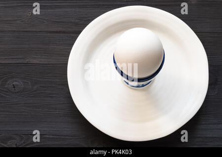 above view of white egg in cup on plate on dark wooden table with blank copyspace Stock Photo