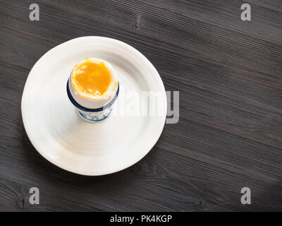 above view of open soft-boiled white egg in cup on plate on dark wooden table with blank copyspace Stock Photo