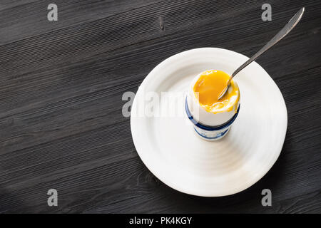 above view of soft-boiled white egg with spoon in cup on plate on dark wood board with blank copyspace Stock Photo