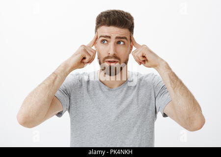 Pull yourself together and think. Portrait of unsure thoughtful worried handsome man with beard and moustache touching temples with fingers looking at upper left corner concerned while thinking Stock Photo