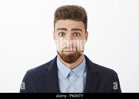 Waist-up shot of silly and gloomy cute brunet boyfriend with blue eyes and beard smirking standing in elegant suit feeling sorry apologizing for being stupid posing against gray background Stock Photo