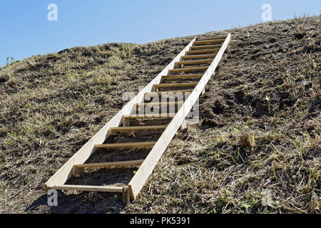 A clumsy wooden ladder lying on an earthen hill. Conceptual - movement up steep inconvenient steps: business, creativity, human development Stock Photo