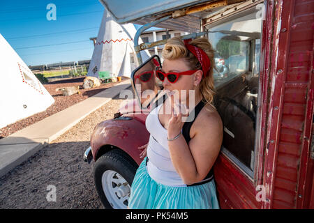 Blonde adult female with a 1950s vintage pin up hairstyle stands near an abandoned vintage car, wearing cat eye sunglasses Stock Photo