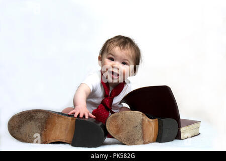 Baby Boy wanting to be like his minister father sits with dad's tie, old shoes and hand on opened Bible.  Christian Sweet Image. Stock Photo