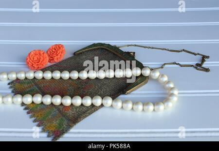 vintage mesh purse with orange vintage earrings and pearl necklace on a white background