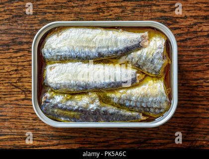 An open can of sardines in oil on a weathered wooden table seen from above. Stock Photo
