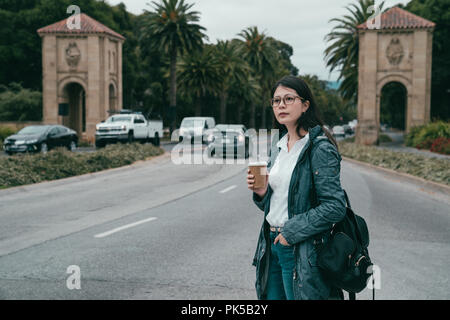 woman standing in front of the entrance of a university with holding a cup of coffee. Stock Photo