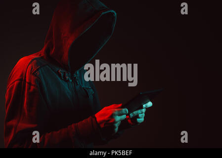 Hooded faceless hacker with tablet computer in cybersecurity concept Stock Photo
