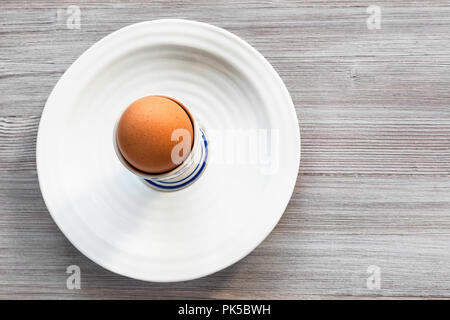 top view of brown egg in cup on white plate on gray wooden board with blank copyspace Stock Photo