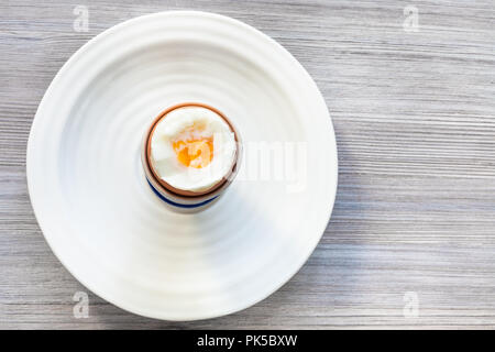 top view of soft-boiled brown egg in cup on white plate on gray wooden board with blank copyspace Stock Photo