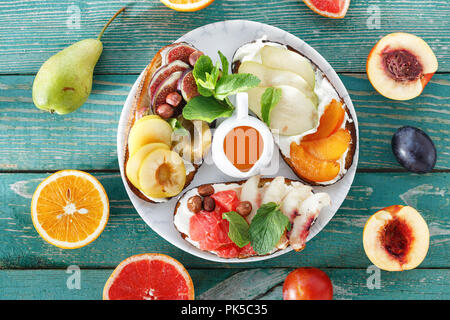 Plate with various fruit bruschetta on green wooden table, top view. Healthy and tasty breakfast concept Stock Photo