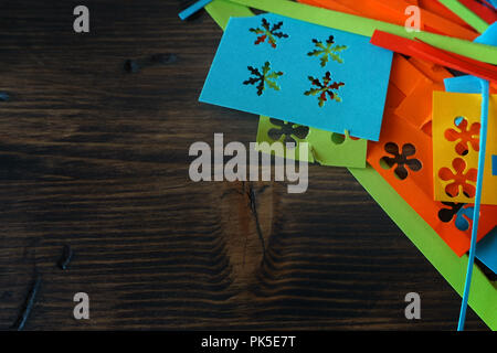 Making homemade bright colorful decorations for a party or Christmas with paper cut outs in a handicraft concept over rustic wood with copy space Stock Photo