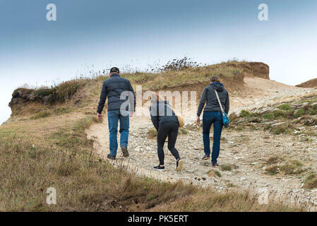 Three people walking along a heavily eroded worn footpath on the coast of Cornwall. Stock Photo