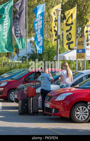 young woman hiring a car and getting it checked over by the attendant assistant at the car hire garage or lot depot. Stock Photo
