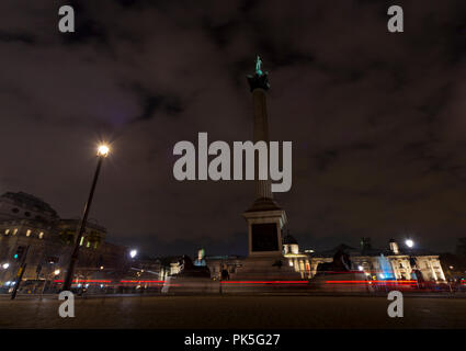 Nelsons Column at night with traffic. Long exposure of traffic passing the bottom of Nelson's Column. Extreme wide angle. Red bus and black taxi cab. Stock Photo