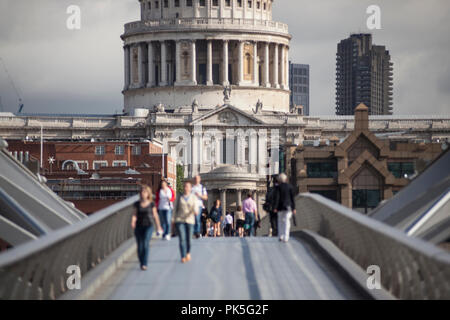 Millennium Bridge looking toward St Paul's Cathedral. People walk over the pedestrian only bridge over the River Thames. Summertime in London.