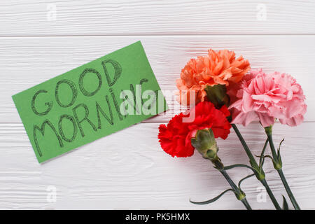 Good morning wish note and colorful carnation flowers. White wood background. Top view. Stock Photo
