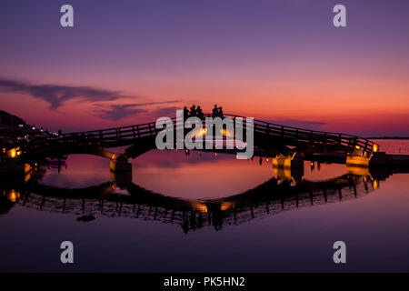 Silhouettes and reflections as tourists enjoying a beautiful sunset over the marina bridge in Lefkada (Lefkas), Greece Stock Photo