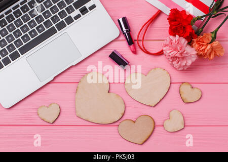 Romantic accessories for woman on pink wood. Flat lay, top view. Laptop, lipstic, flowers and heart shaped wooden hearts. Stock Photo